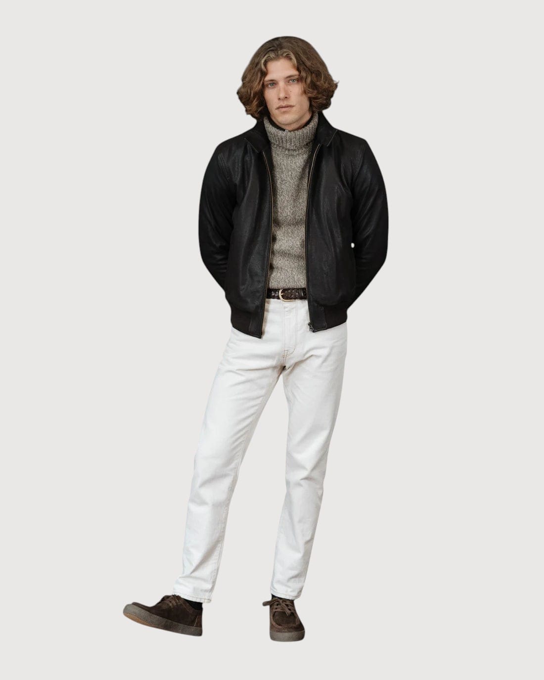 A man wearing a Luxequir Vogue deep earth leather bomber jacket with ribbed cuffs over a grey turtleneck and jeans.